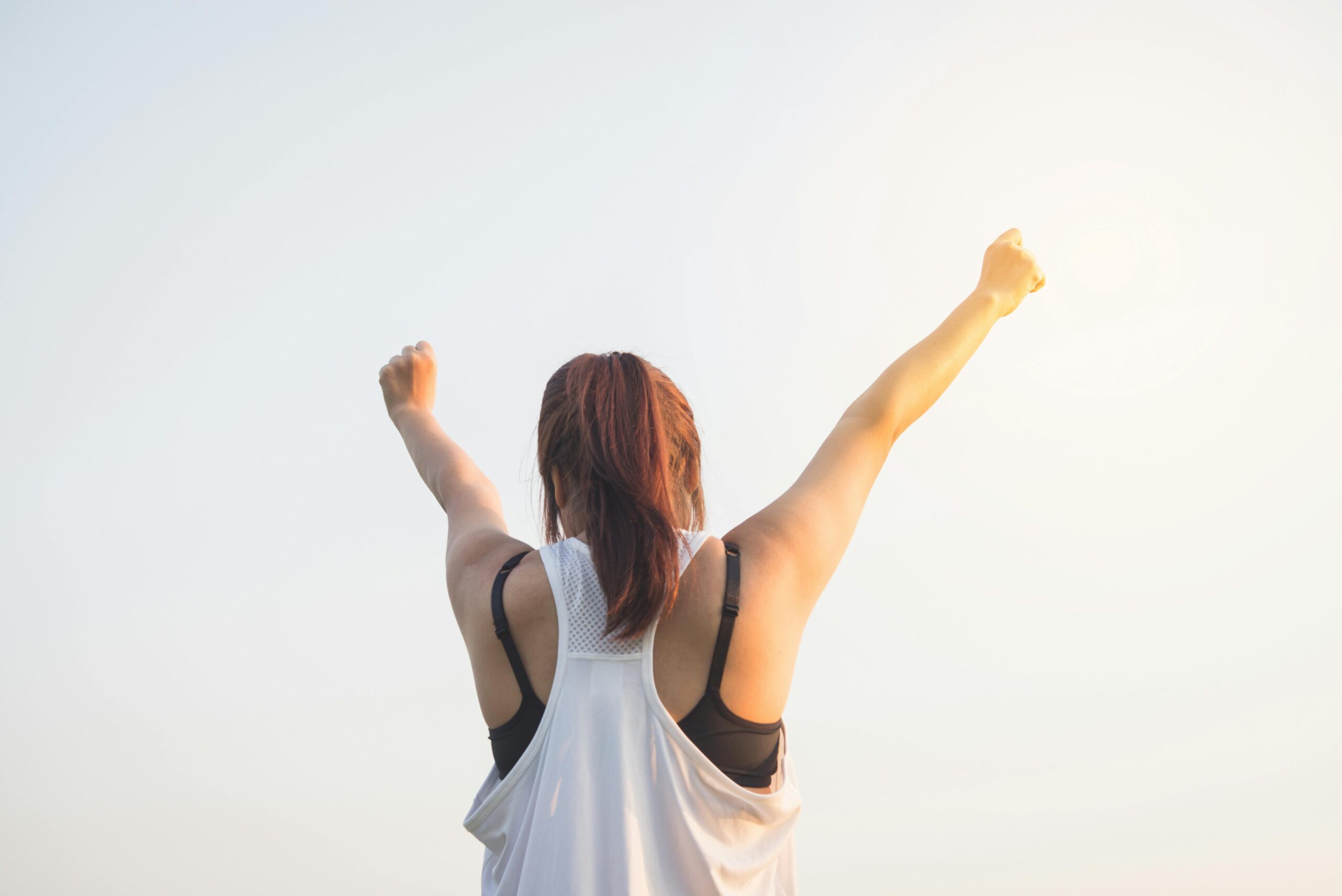 A woman celebrates success with arms raised in a bright outdoor setting.